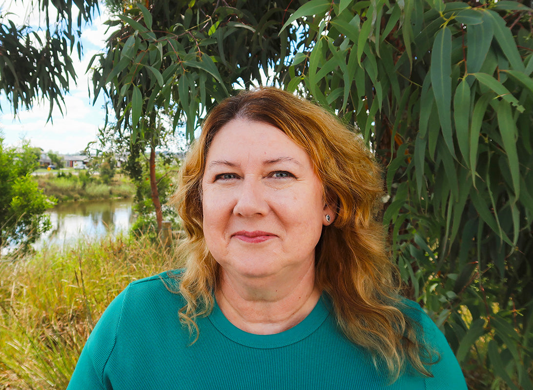 Leonie standing outdoors with a creek and eucalyptus tree in the background.